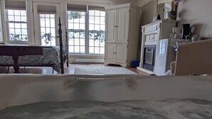 A room with a large bathtub, a dining table, and a view of the outdoors through large windows. - Annapolis Suite - Private HotTub, KingBd, DT (Wolfville)
