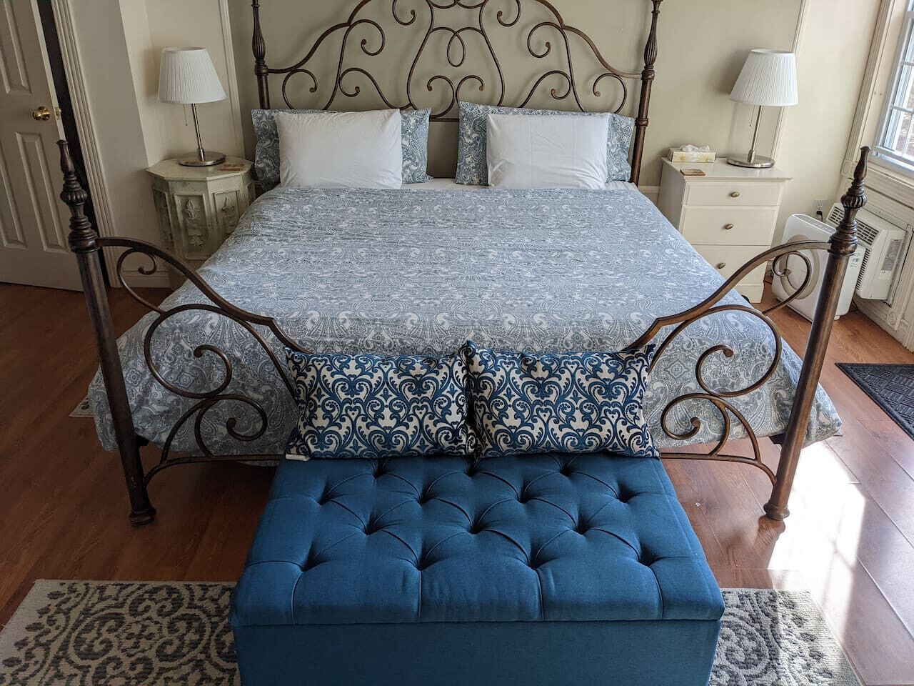 A bed with a patterned bedspread and pillows, a blue upholstered bench, and a metal headboard.