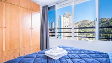 A bedroom with a large bed, wooden wardrobe, and a window with a city view.