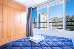 A bedroom with a large bed, wooden wardrobe, and a window with a city view. - Tropic Mar Apartment 15A Levante Beach (Benidorm)