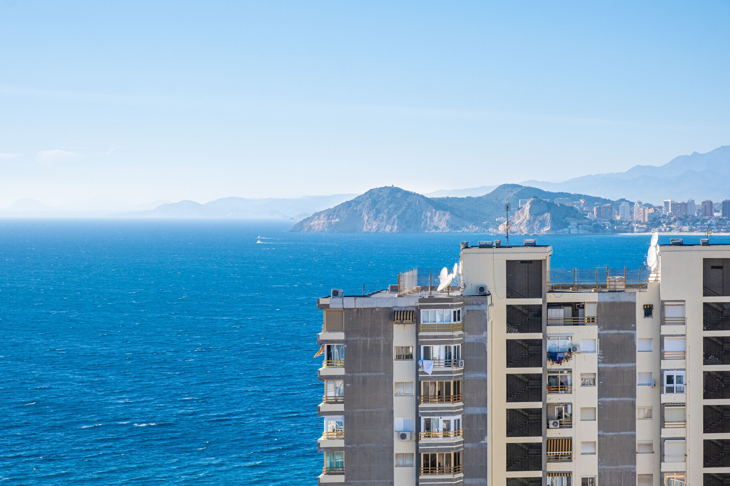 A high-rise building with balconies overlooking a coastal cityscape and the sea.
