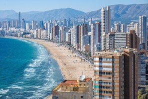 Paesaggio costiero con grattacieli, una spiaggia sabbiosa e un mare blu limpido.