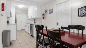 A compact kitchen with white cabinets, a dining table with chairs, and a small trash bin. - Artsy Room with Free Parking (Miami)