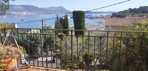 Ein Balkon mit Blick auf einen Jachthafen, ein Berg im Hintergrund und ein Gebäude mit einem Ziegeldach.