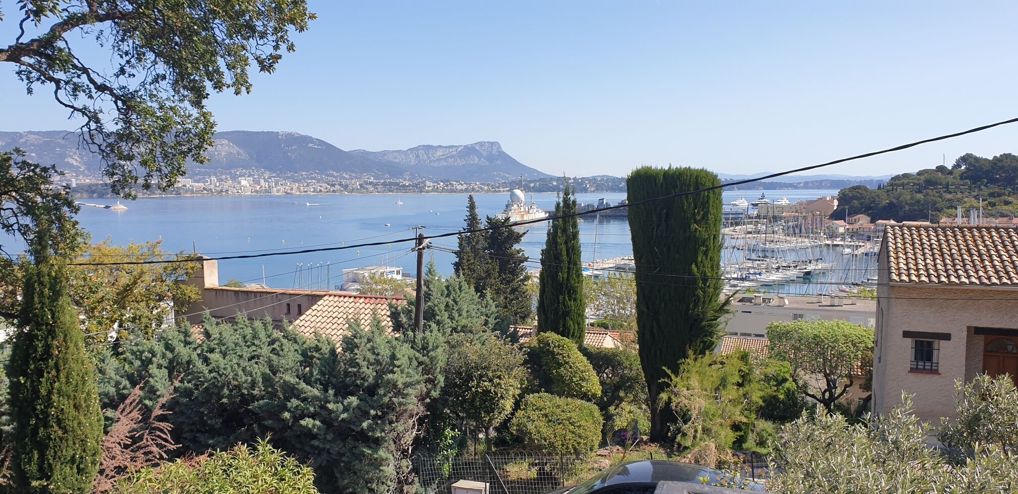 Paesaggio costiero con una marina, edifici e una montagna sullo sfondo.