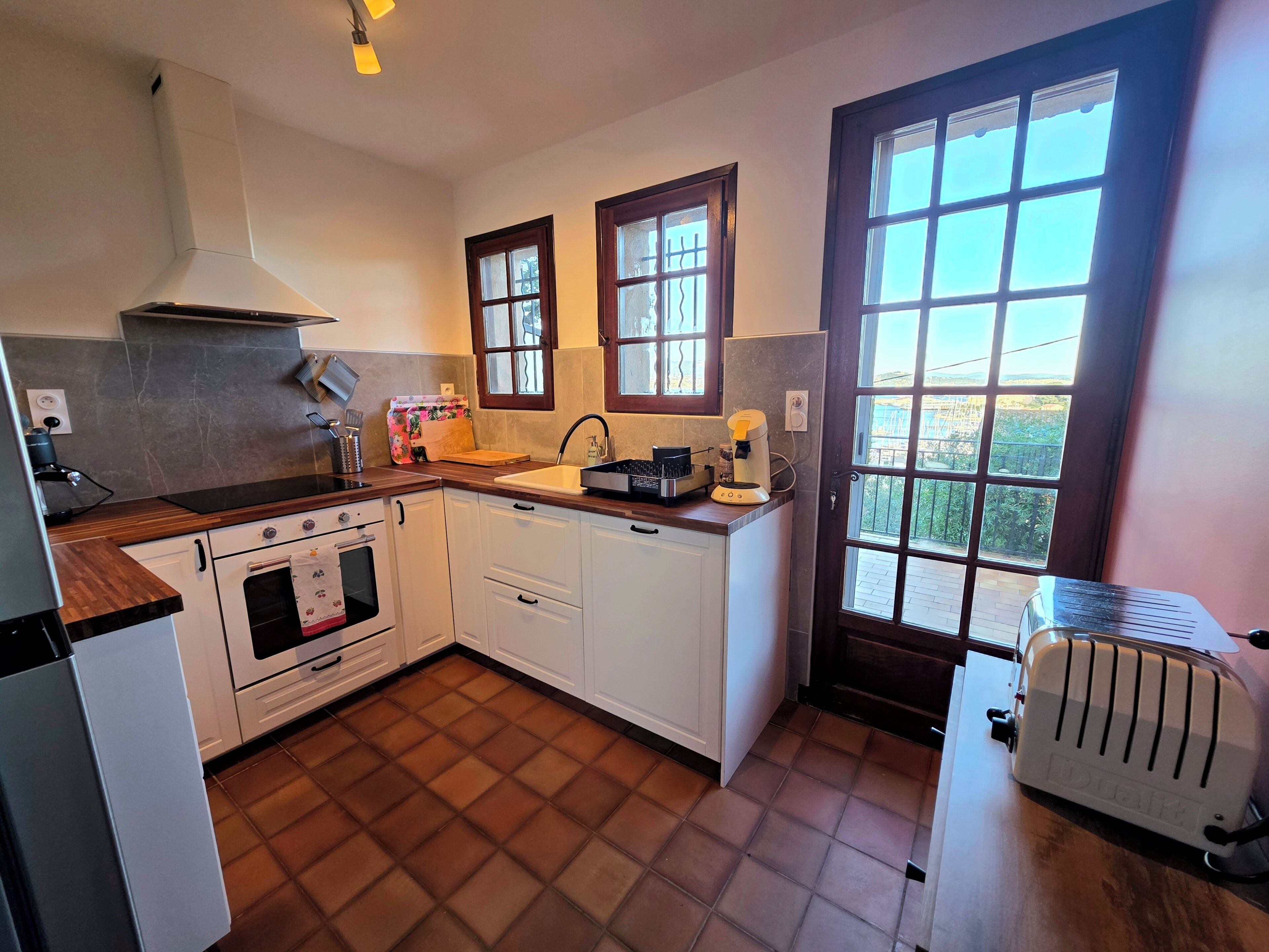 A kitchen with a stove, oven, sink, and a toaster. There are windows and a view outside.