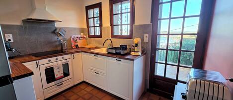 A kitchen with a stove, oven, sink, and a toaster. There are windows and a view outside.