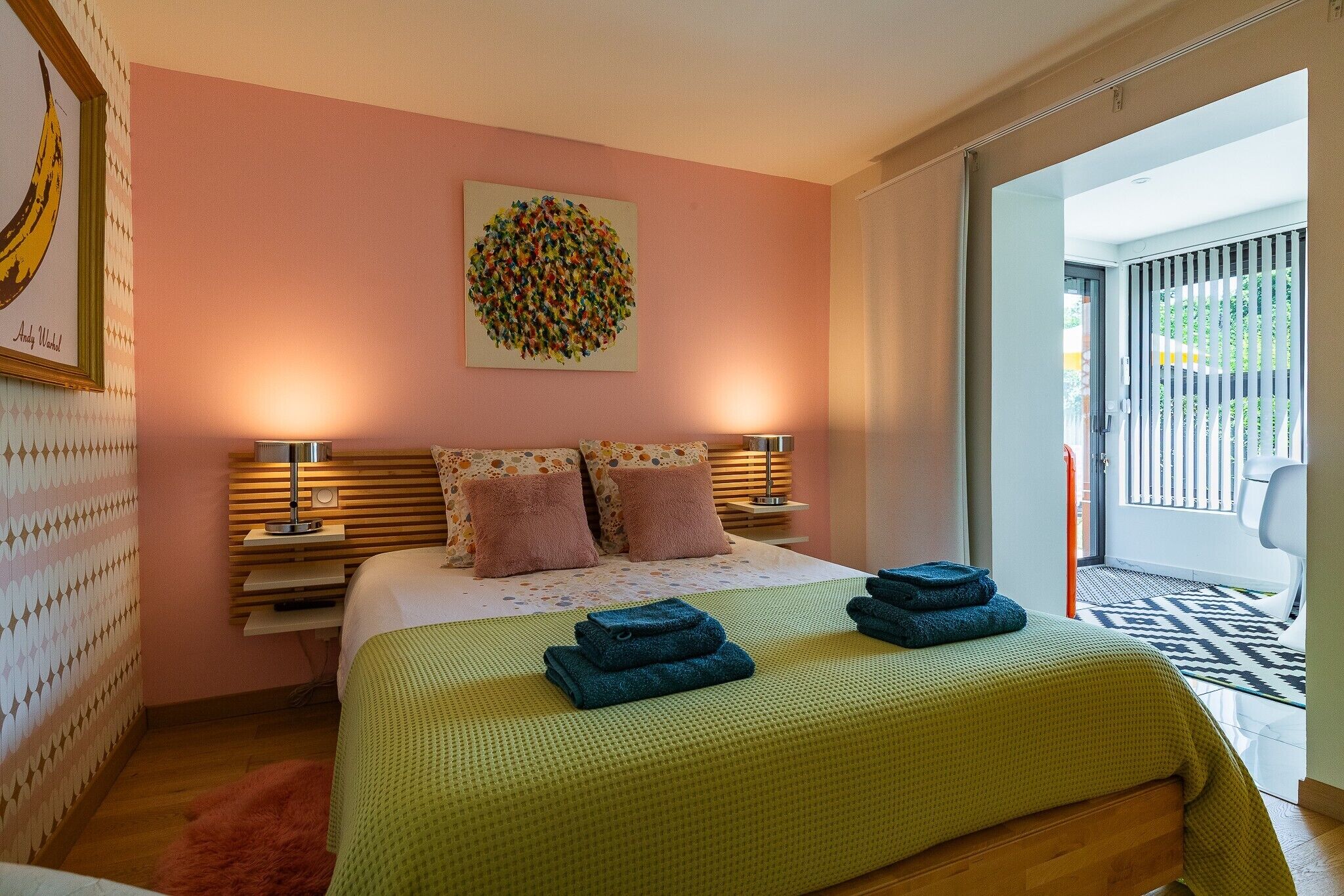 A bedroom with a bed, pillows, a wall art piece, a nightstand, and a view through a sliding door.
