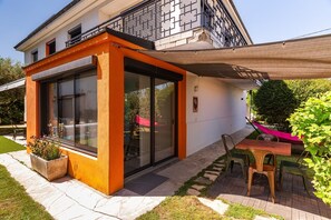 Une maison moderne avec une entrée dotée d’une porte en verre, un petit espace extérieur aménagé avec une table et des chaises, et un jardin agrémenté d’un jardinière.