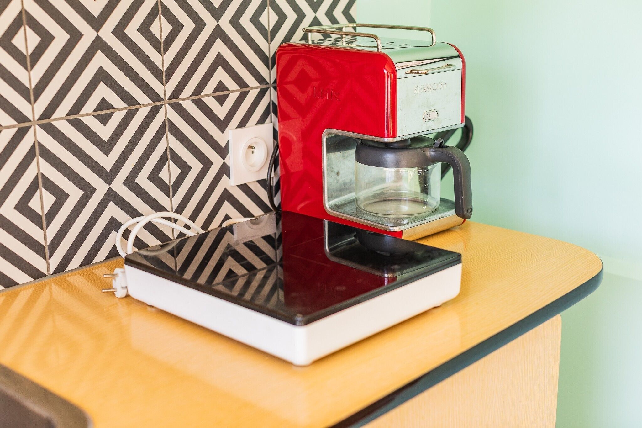 A red coffee maker on a wooden counter with a patterned wall in the background.