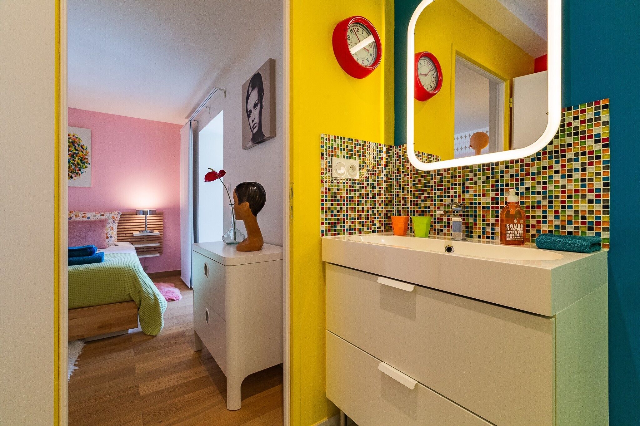 A room with a bed, a dresser, a mirror, and a colorful tiled wall.