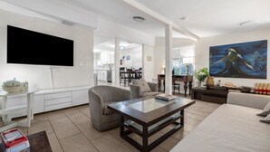 Un salon moderne avec un téléviseur à écran plat, un grand tableau et un coin repas à l’arrière-plan.