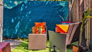 Un espace patio aménagé avec des meubles en osier, une petite table sur laquelle est posé un vase, et une bâche bleue en arrière-plan.