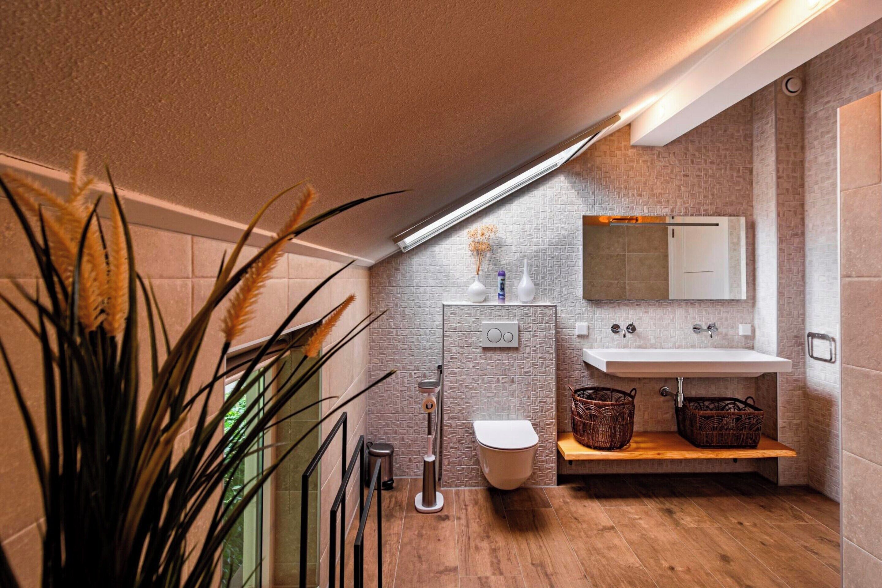 Een moderne badkamer met een wit wastafel, toilet en douchegedeelte. Er staan rieten manden op een plank en een plant in de hoek.