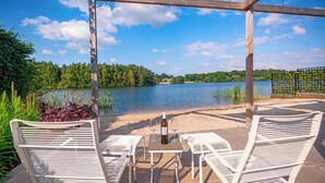 Ein Sitzbereich im Freien mit Tisch und zwei Stühlen, mit Blick auf einen See, überdacht von einer hölzernen Pergola.