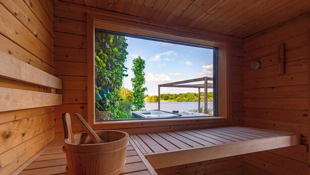 Eine Holzsauna mit großem Fenster, Holzbänken und einem Holzfass.