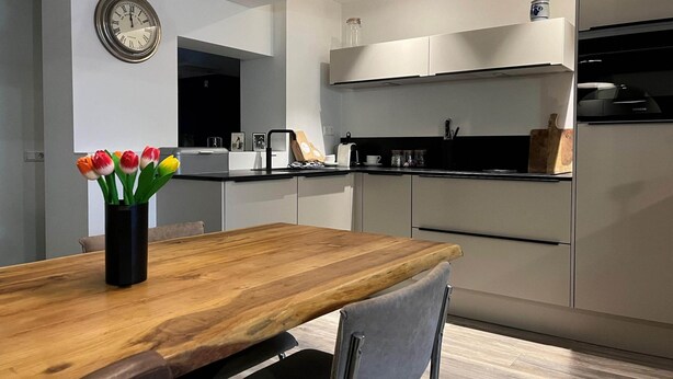 Eine moderne Küche mit einem Holztisch, einer Uhr und einer Tulpenvase.