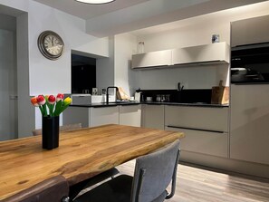 A modern kitchen with a wooden dining table, a clock, and a vase of tulips. - Beach Haven in Egmond Center (Egmond aan Zee)