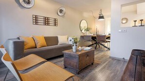 Ein modernes Wohnzimmer mit einer Couch, einem Couchtisch und Sesseln. Im Hintergrund ist eine Essecke mit Tisch und Stühlen zu sehen.
