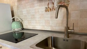 Una cocina con un lavamanos de acero inoxidable, una tetera y una placa de inducción negra.