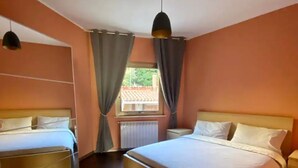 Una habitación de hotel con dos camas, una ventana con cortinas, un radiador y una lámpara colgante.