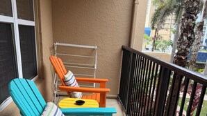 A balcony with two chairs and a small table, a metal railing, and a view of a residential area with palm trees and buildings. - Pool- BeachSide- Pet Friendly- 2-3min walk to beach. (South Padre Island)