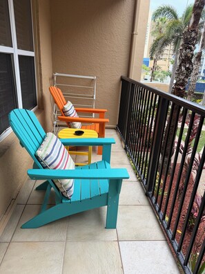 Ein Balkon mit zwei Stühlen und einem kleinen Tisch, einem Metallgeländer und Blick auf eine Wohngegend mit Palmen und Gebäuden.