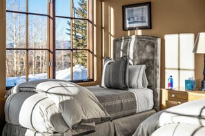 Un dormitorio con cama, mesita de noche, cuadro enmarco y ventana con vistas a árboles y montañas.