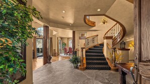 A spacious foyer with a stone floor, a wooden staircase, and a large plant.