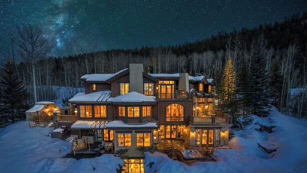 A large, multi-story lodge with a snow-covered landscape, illuminated windows, and a view of the night sky.
