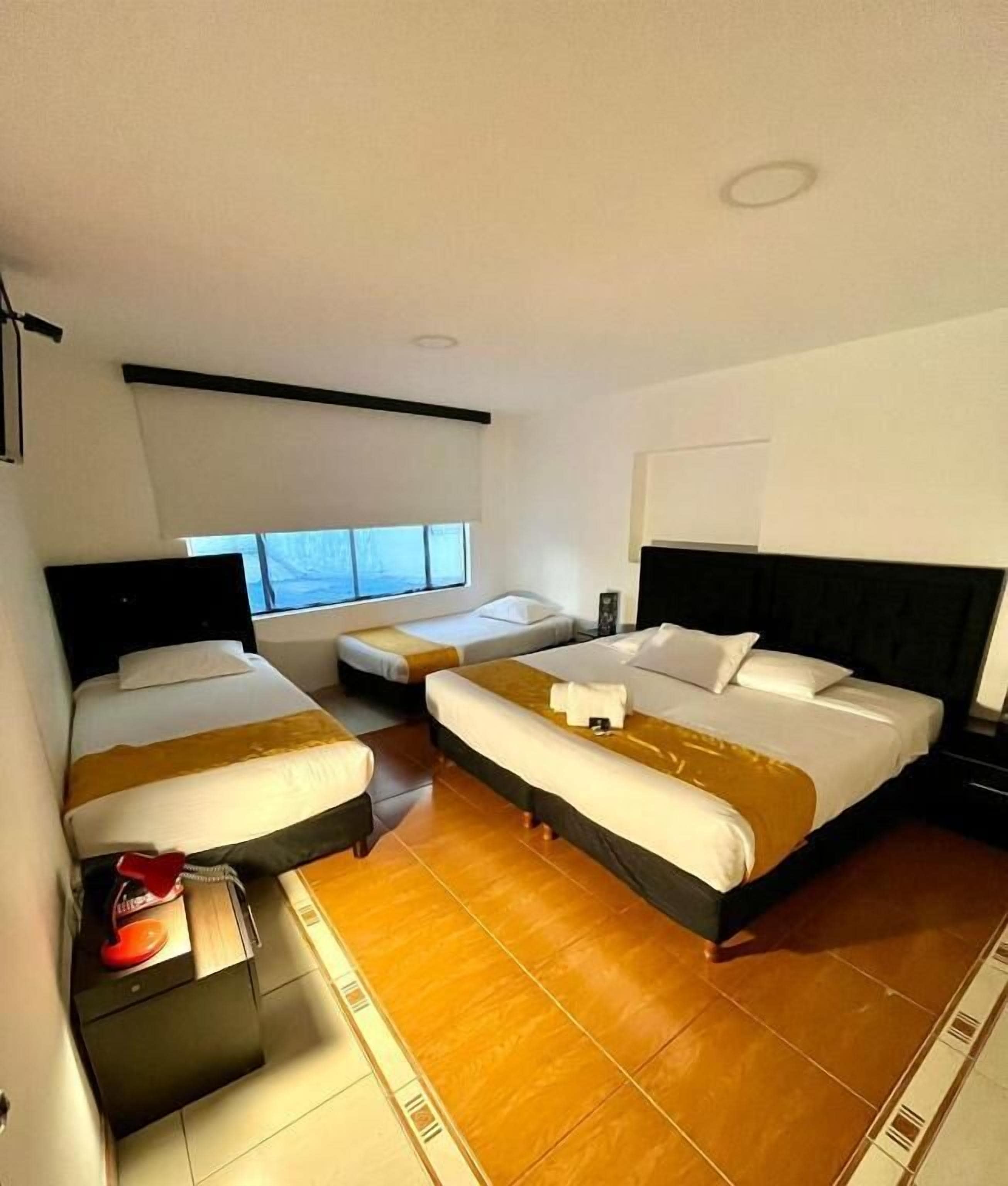 A hotel room with three beds, a small table, and a window.
