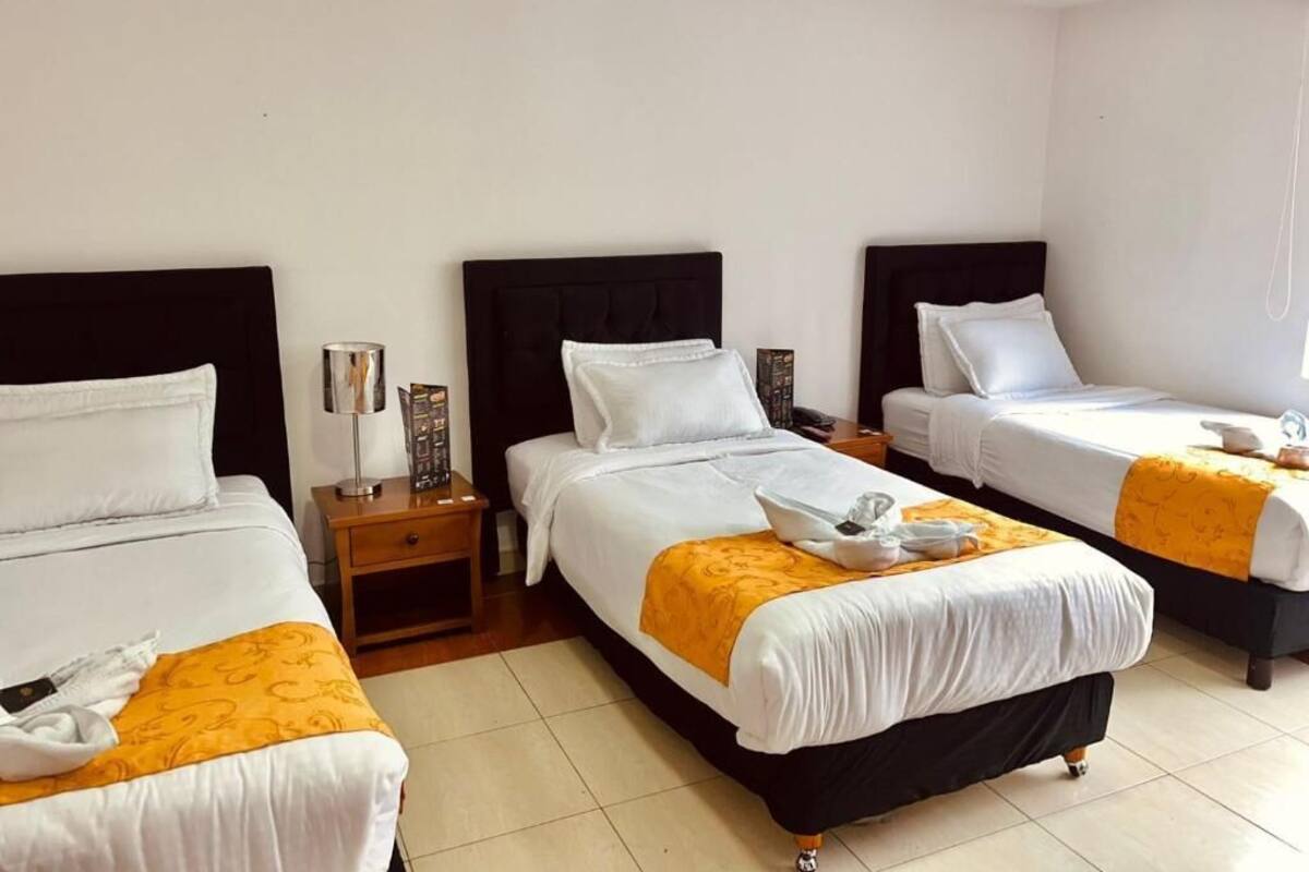 Una habitación de hotel con tres camas, una mesita de noche y una lámpara.