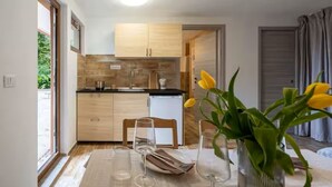 Una cocina moderna con armarios de madera, un refrigerador pequeño y una zona de comedor con una mesa dispuesta para dos.