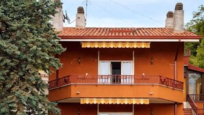 Un edificio de dos pisos con techo de tejas rojas, entrada con reja y un balcón en el piso superior.