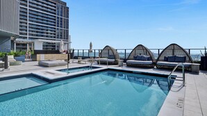 Una piscina sul tetto con zone relax e vista su un grattacielo.