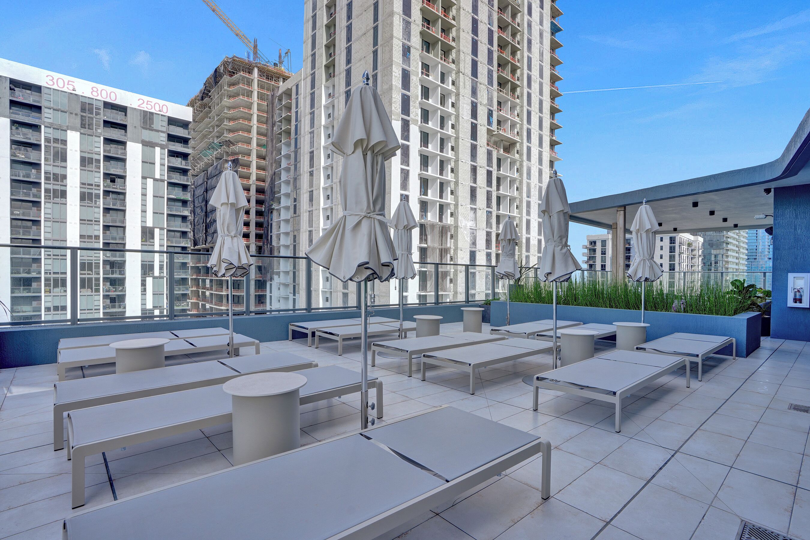 Een terras op het dak met witte tafels en parasols, een hoog gebouw op de achtergrond en een helderblauwe lucht.