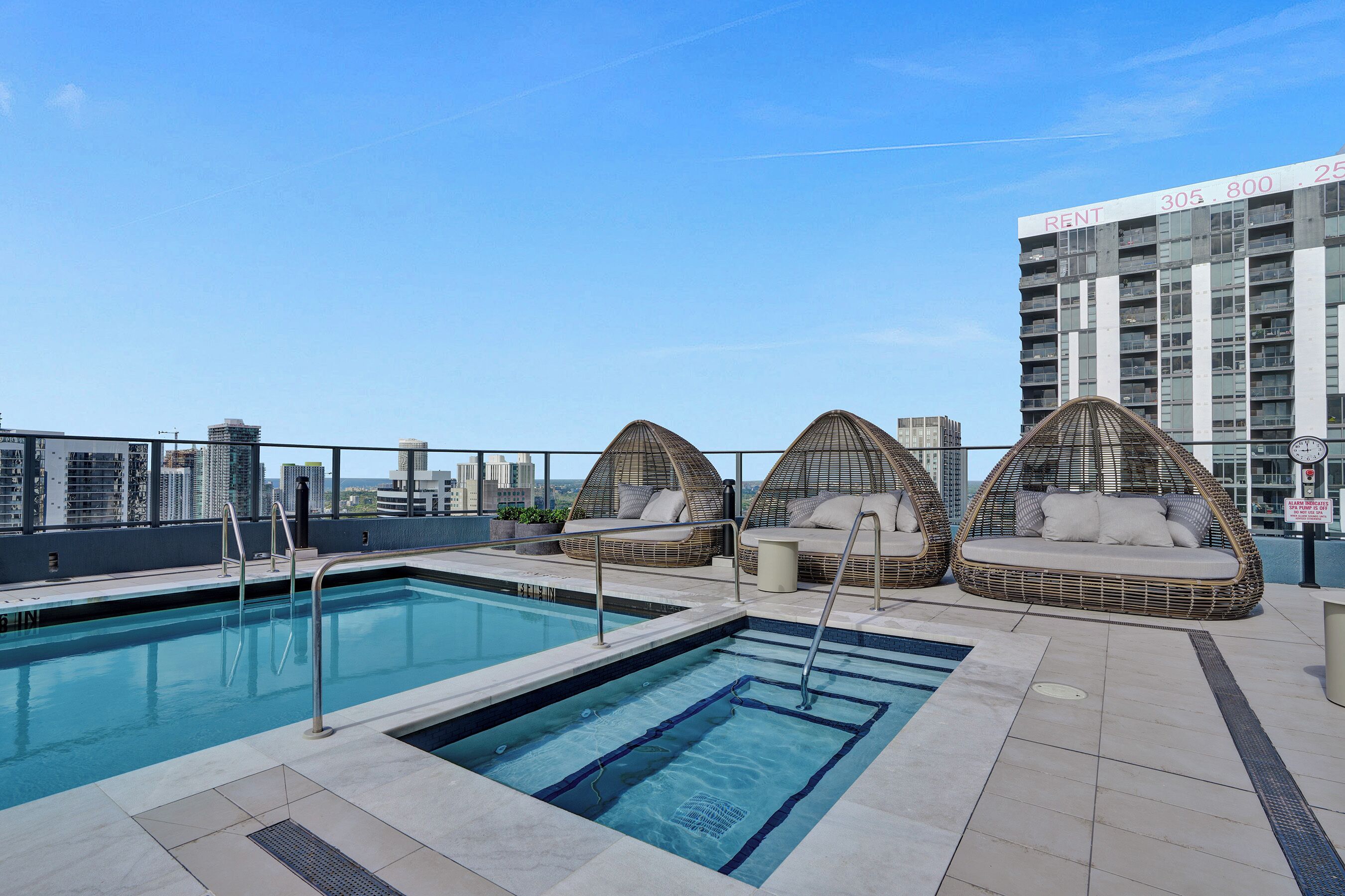 A rooftop pool with two wicker lounge chairs and a view of a high-rise building.