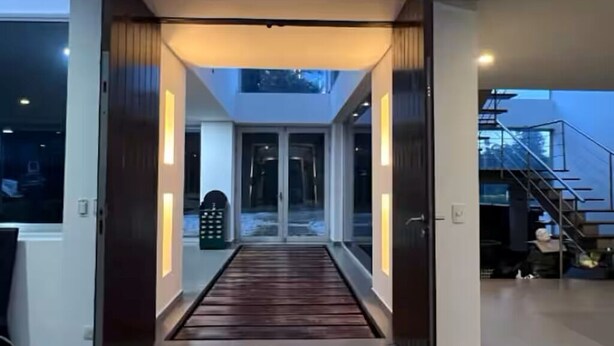 Ein modernes Interieur mit einem offenen, zentralen Bereich, Glastüren zu einer unteren Ebene und einer Treppe rechts.