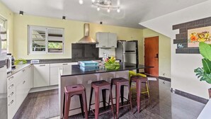 A modern kitchen with a central island, bar stools, a stainless steel refrigerator, and a window with a view. - Modern Villa with Pool & Garden (Moorea-Maiao)