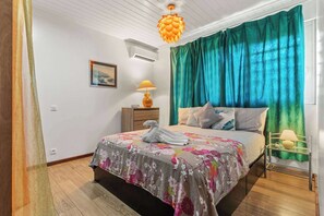 Une chambre à coucher comprenant un lit, une table de chevet, une lampe, une fenêtre avec des rideaux et un luminaire suspendu.