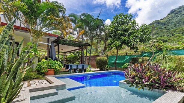 A swimming pool with steps leading into it, surrounded by tropical plants and a covered patio area. - Modern Villa with Pool & Garden (Moorea-Maiao)