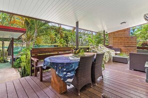 Une terrasse extérieure dotée d’un plancher en bois, de meubles en osier et d’une table recouverte d’une nappe bleue.