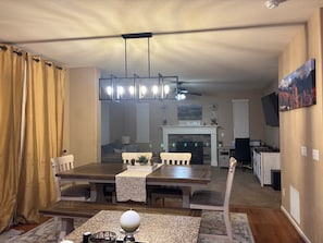 Un comedor con una mesa de madera, sillas, una araña, una chimenea y un televisor en la pared.