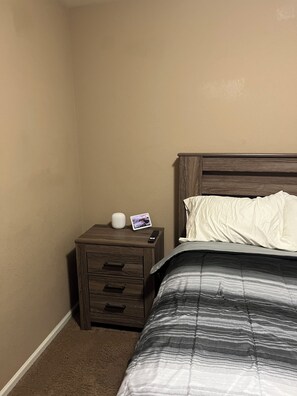 Ein Schlafzimmer mit Bett, Nachttisch, Fernbedienung und einem kleinen elektronischen Gerät.