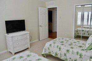 Ein Schlafzimmer mit Fernseher auf einer Kommode, einem Bett mit gemustertem Überwurf und einem Schrank mit Spiegel.