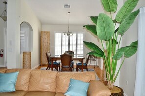 Ein Wohnzimmer mit einem Ledersofa, einem Esstisch mit Stühlen und einer großen Pflanze.