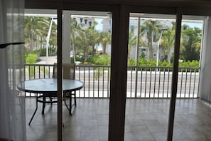 Ein Balkon mit rundem Tisch und Stühlen, Blick auf eine Straße mit Palmen und ein Gebäude im Hintergrund.