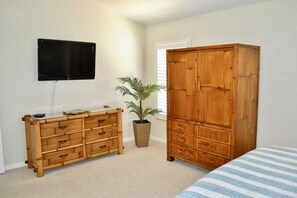 Ein Schlafzimmer mit einem Bett, einem Holzschrank, einem an der Wand befestigten Fernseher und einem Blumentopf.