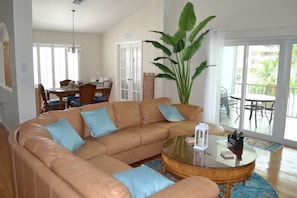 Ein Wohnzimmer mit einem großen, sandfarbenen Ecksofa, einem Glastisch und einer üppigen Pflanze.