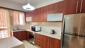Una cocina con armarios de madera, un refrigerador de acero inoxidable, un microondas y una mesa con una silla.